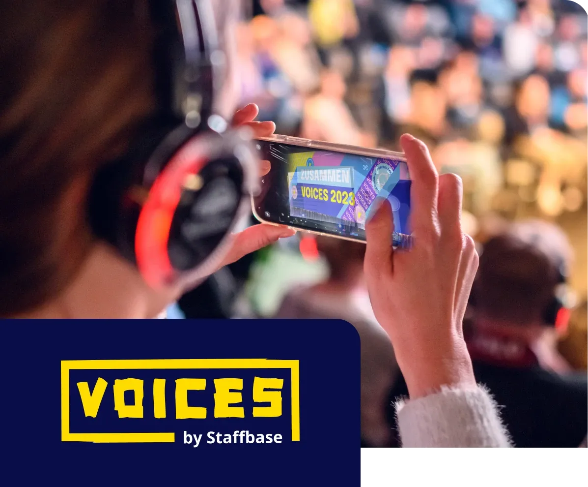 Person wearing headphones records a blurred event on their phone. "VOICES 2023" is visible on the screen. Event logo in the corner.