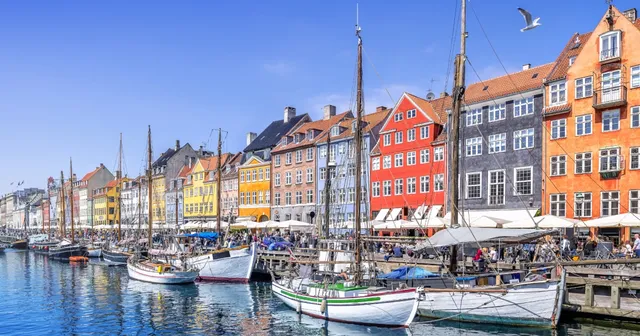 Colorful buildings line the waterfront at Nyhavn in Copenhagen, with boats docked along the canal under a clear blue sky.