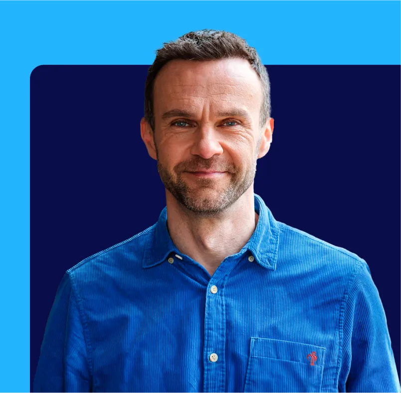 Man in a blue shirt smiling against a blue and navy geometric background.